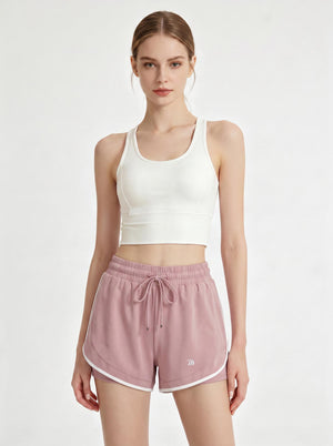 A woman stands in a studio wearing a white cropped athletic tank top and #pink 2 in 1  running shorts.