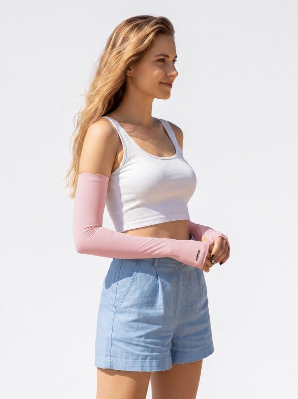 A woman wearing a sun protection white crop tank top, light blue shorts, and light pink long arm sleeves, standing against a solid white background.
