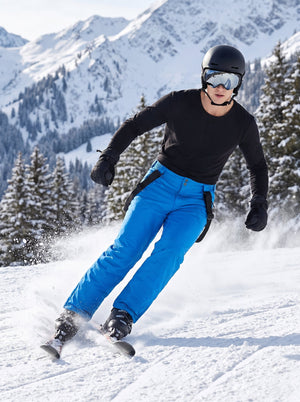 Male skier riding on snowy mountain slope, wearing #royalblue men's ski bib pants with detachable black suspenders, black helmet and ski goggles, snow splashing around, winter alpine landscape background, commercial outdoor sport product photo for men's snow trousers