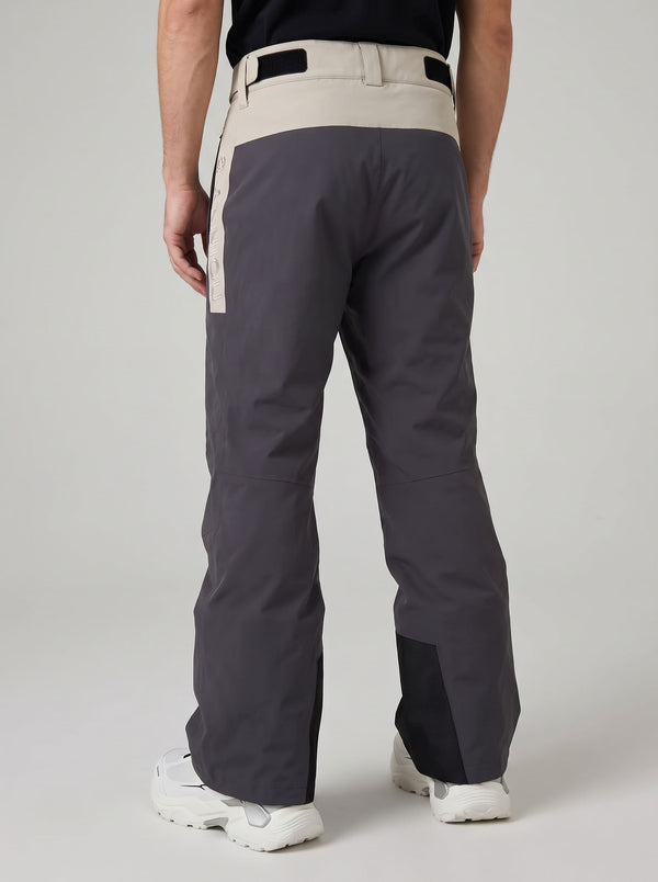 Rear view of a person wearing dark gray heated ski pants with a light beige waistband and side panel, paired with white ski boots