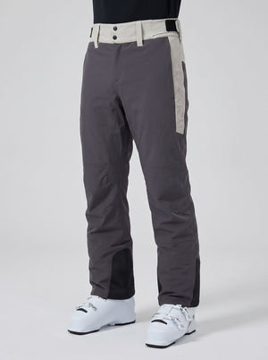 Dark gray ski pants with beige side panels and a matching beige waistband, shown on a model wearing white ski boots against a light gray studio background.