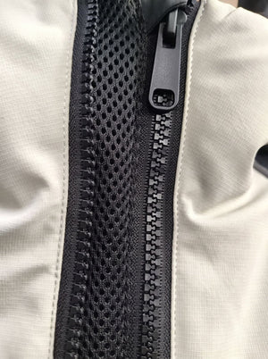 Close-up of a black mesh zipper panel on a light beige or off-white fabric ski jacket, showing the black zipper teeth and pull tab.