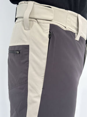 Close-up of a pair of color-blocked snowboard pants with a light beige waistband and side panel, a dark gray vertical stripe, and a dark gray zippered pocket on the thigh.