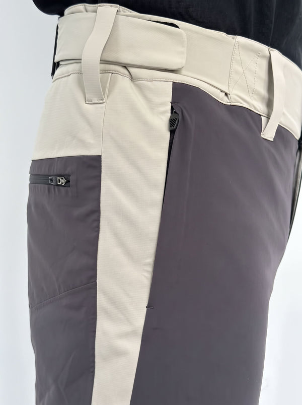Close-up of a pair of color-blocked snowboard pants with a light beige waistband and side panel, a dark gray vertical stripe, and a dark gray zippered pocket on the thigh.