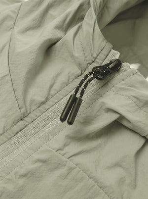 Close-up of a light sage green lightweight jacket with a black drawstring zipper.