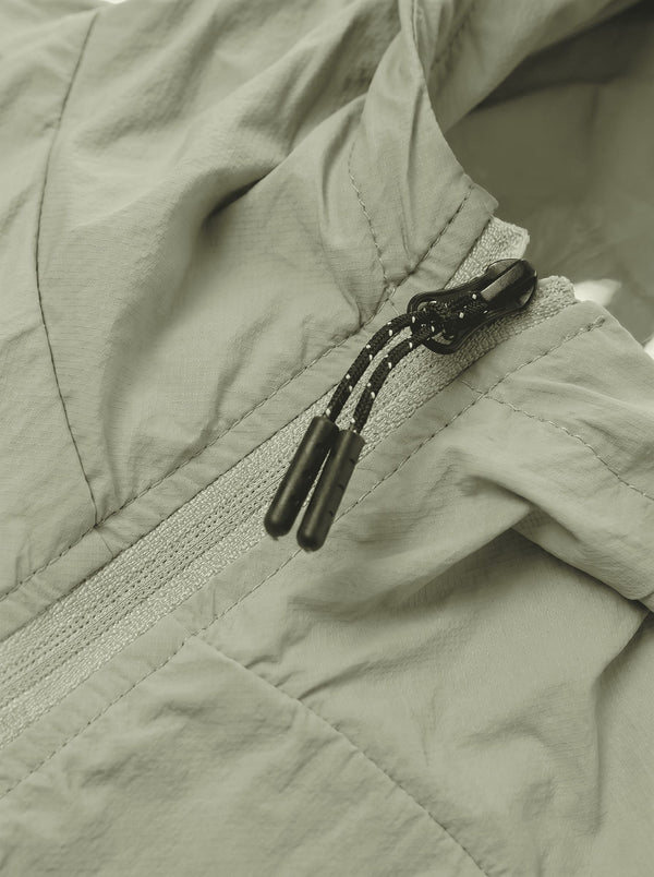 Close-up of a light sage green lightweight jacket with a black drawstring zipper.