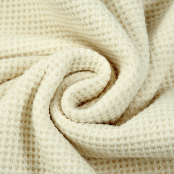 Close-up view of rolled cream waffle knit fabric showcasing its textured grid pattern.