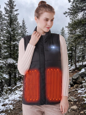 young woman wearing black heated vest with glowing orange heating‑zone outlines, snowy pine‑forest outdoor background, adjusting vest collar, LED control button on chest, cold winter mountain scenery.