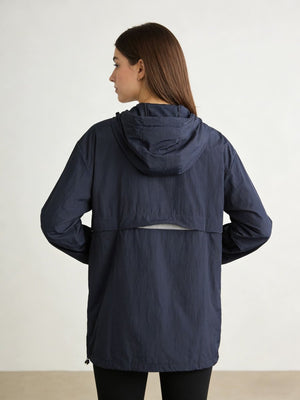 A woman shown from the back wearing a navy blue hooded jacket against a plain light studio background.