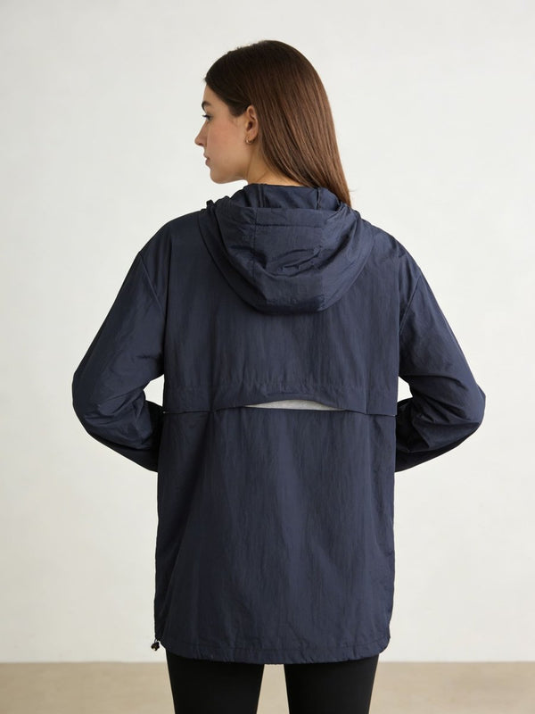 A woman shown from the back wearing a navy blue hooded jacket against a plain light studio background.