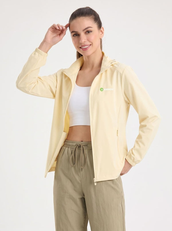 A woman modeling a #lightyellow lightweight zip-up hooded athletic jacket over a white sports bra and olive green drawstring pants, photographed against a plain light gray studio background.