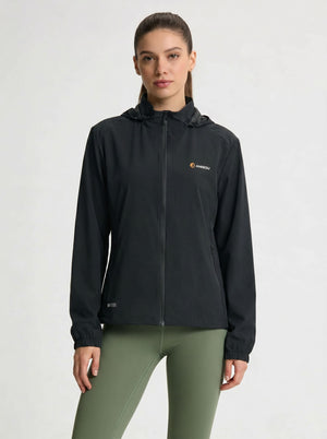 A woman modeling a #black hooded zip-up athletic jacket with a small orange and white Kari Traa logo on the left chest, paired with olive green leggings, against a light gray studio background.