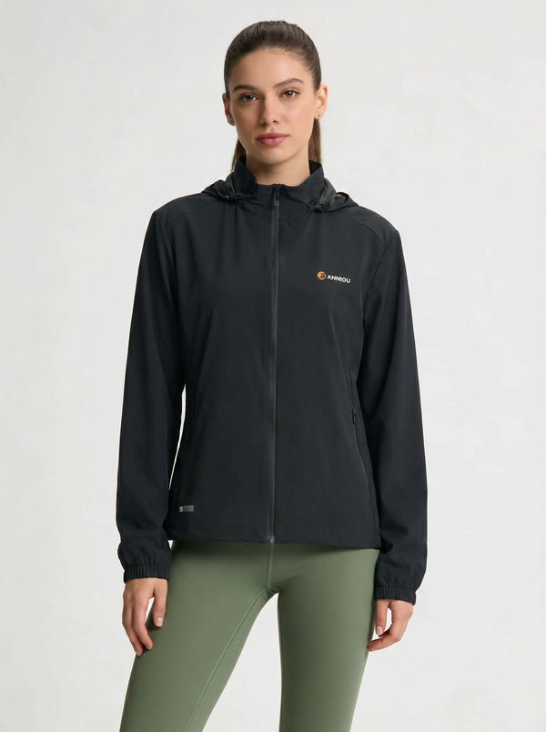 A woman modeling a #black hooded zip-up athletic jacket with a small orange and white Kari Traa logo on the left chest, paired with olive green leggings, against a light gray studio background.