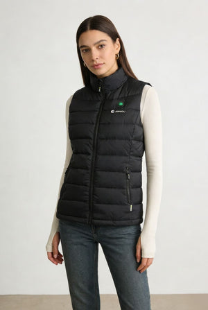 A woman modeling a black heated puffer vest over a cream long-sleeve top and blue jeans.