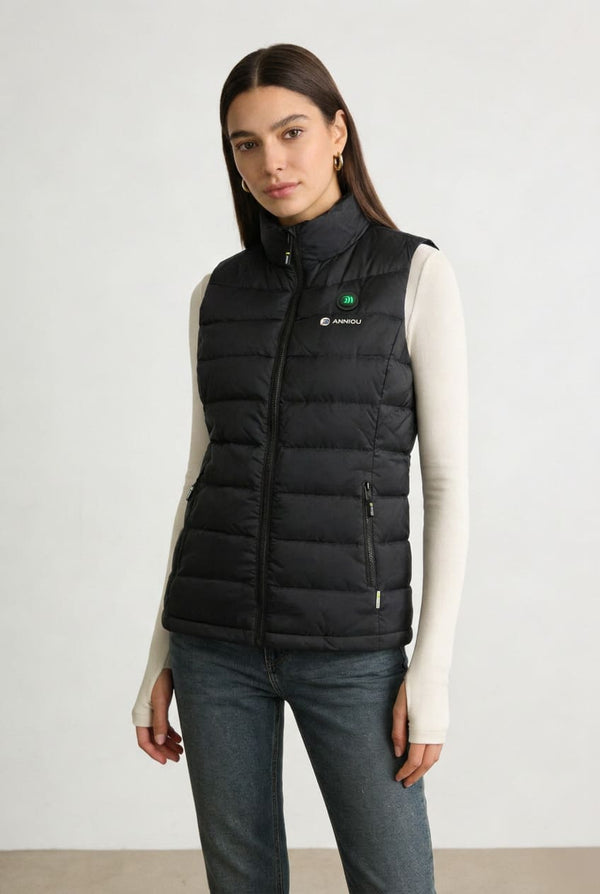 A woman modeling a black heated puffer vest over a cream long-sleeve top and blue jeans.