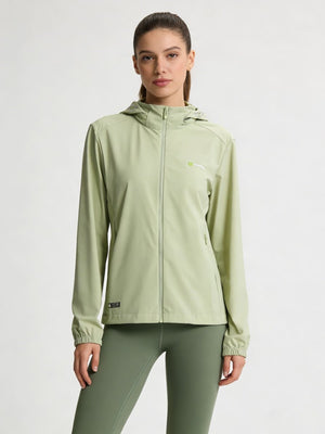 A woman modeling a #lightgreen hooded athletic jacket with a full zipper and matching sage green leggings against a plain light gray studio background.
