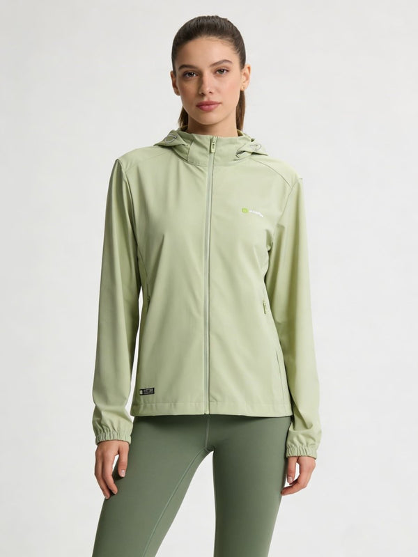 A woman modeling a #lightgreen hooded athletic jacket with a full zipper and matching sage green leggings against a plain light gray studio background.