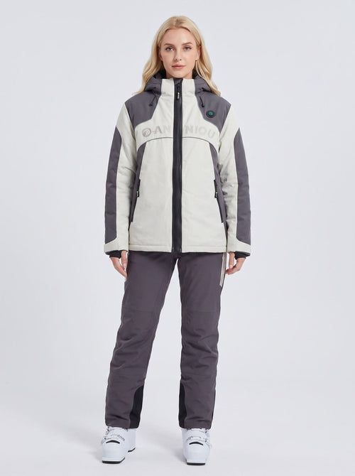 A woman modeling a heated ski jacket and matching ski pants set. The jacket is off-white and dark gray with a black zipper and 'ANNIOU' printed across the chest.