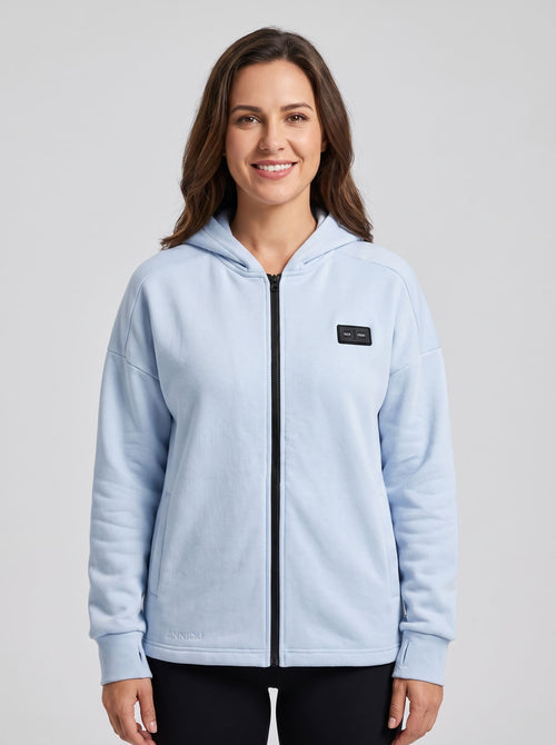 A woman wearing a light blue 5 zone zip-up hoodie with a black front zipper and a small dual switch on the chest.