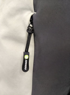 Close-up of a black zipper pull tab with a bright green circular logo and white vertical text reading 'ANNIOU' on a light gray fabric next to a dark gray panel.